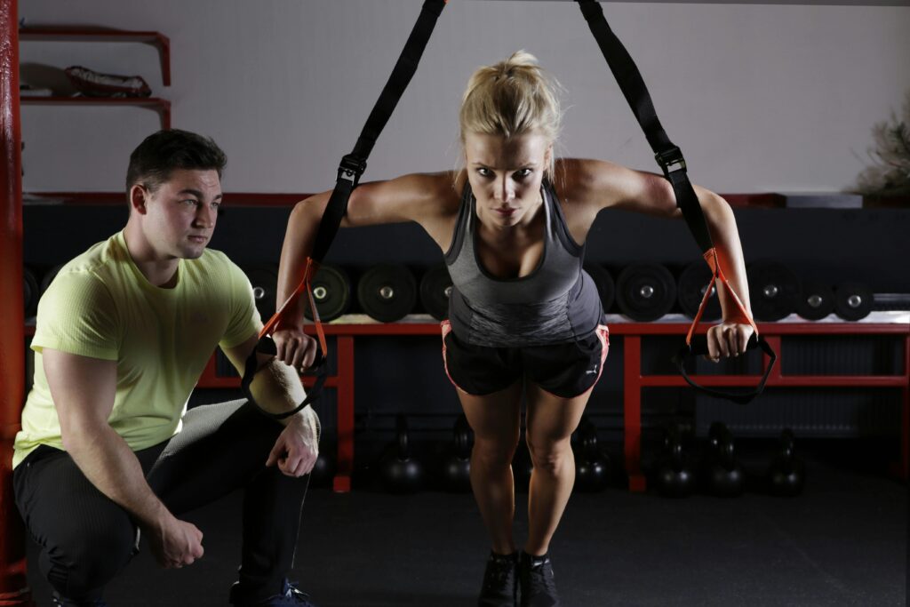 pexels photo 414029 414029 A woman performing strength training with a trainer in a gym setting, showcasing fitness and dedication.